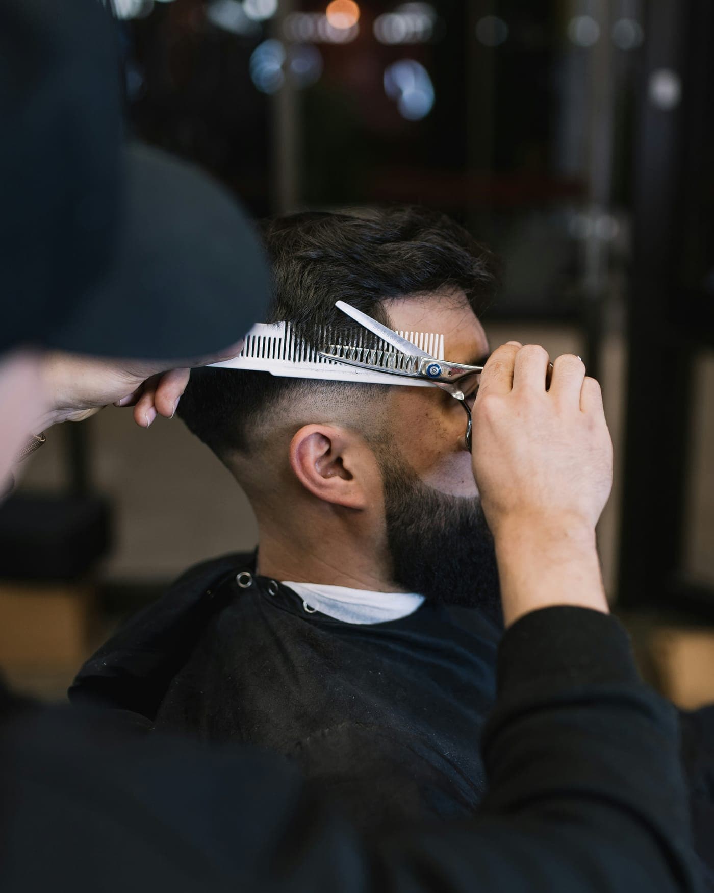 A barber trimming a client's hair with scissors and a comb