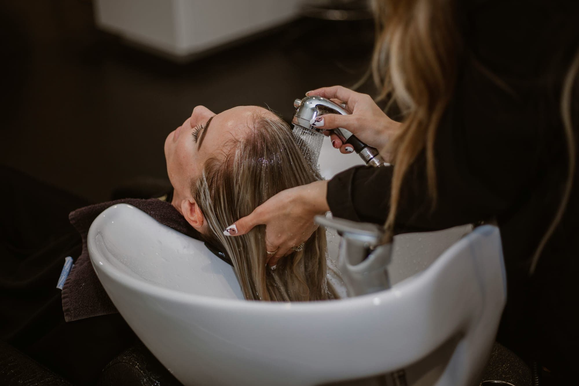 A stylist rinsing a client's hair at a salon basin
